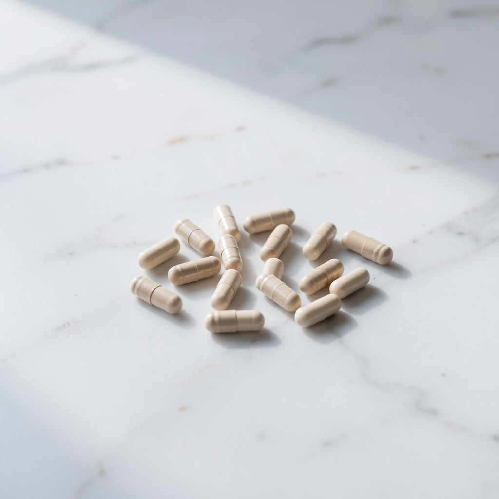 Small supplement capsules on white marble surface with a clean editorial arrangement, soft natural light from left side